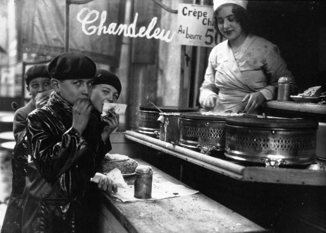 Paris, 1933: children in berets eat crêpes at a Chandeleur street vendor